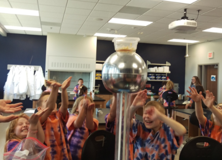 Second graders hold their hands in the air during a science demonstration. 