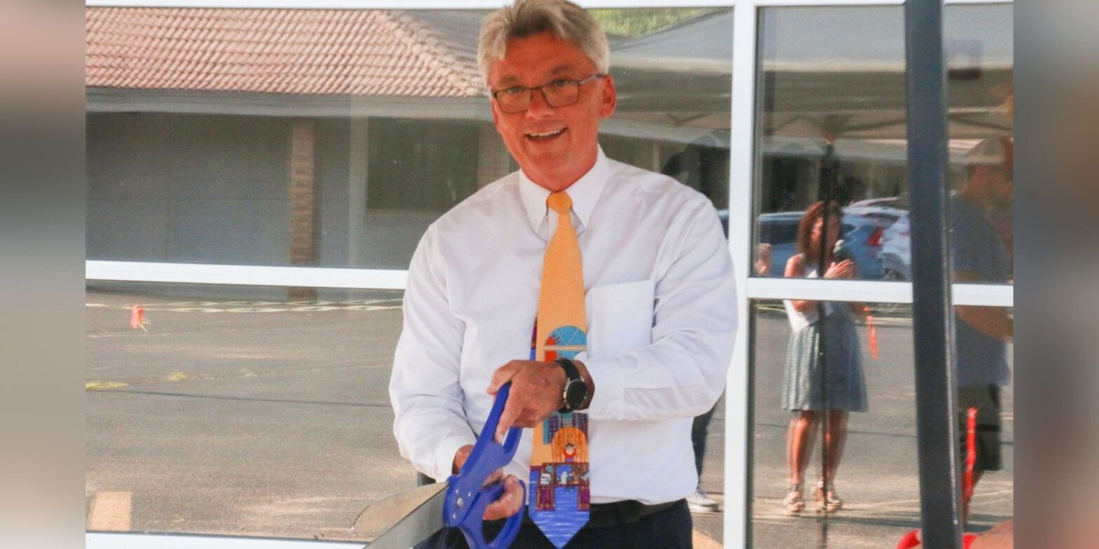 Dr. John Burke holds a pair of giant scissors at the building dedication ceremony.