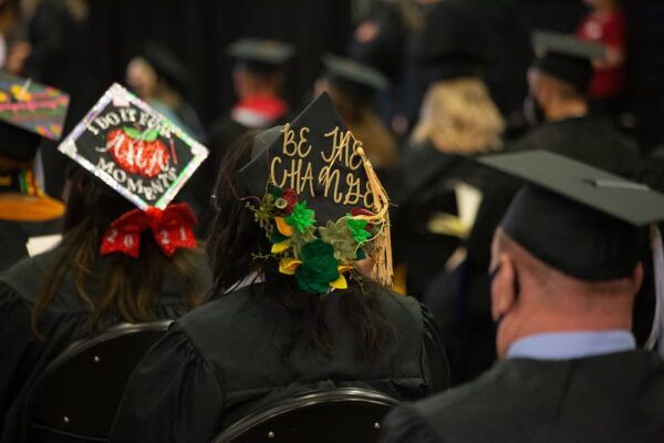 A graduate's graduation cap is decorated with the words "Be the change."