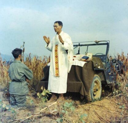 Father Emil Kapaun offers Mass with a fellow soldier using the hood of his Jeep as an altar.