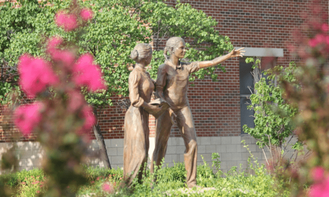 A sculpture of Saint Maria DeMattias and a student resides outside of DeMattias Hall.