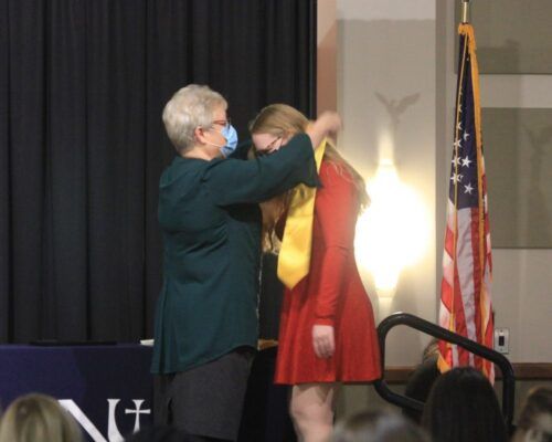 Teresa Vetter gives a newly pinned graduation stole to a nursing graduate.