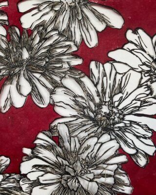 A close up of one of Resnick's works. The artwork displays white flowers outlined in black with a deep red background.
