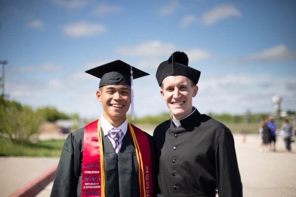 Newman graduate Steven Nguyen and Father Adam Grelinger take a photo together following the commencement ceremony outside Hartman Arena.