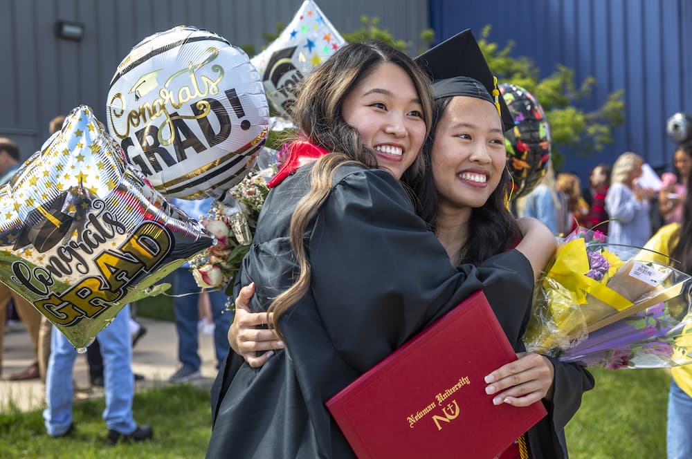 Two Newman graduates hug outside of Hartman Arena during Commencement May 6.