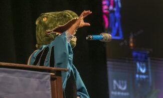 Straub, wearing a dinosaur head, drops an inflatable microphone following his speech at the Newman University graduation ceremony May 6.