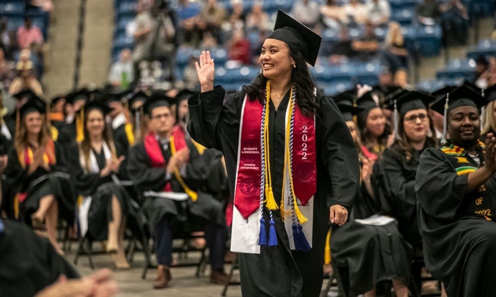 Kelly Mai waves and walks toward the commencement stage to accept her 2022 Newman Ablah Award.