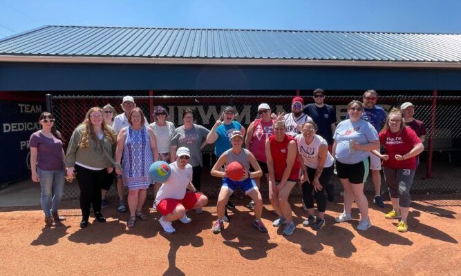 Newman staff versus faculty kickball game to celebrate the end of a successful academic year. Melissa Castle holds a red kickball in the center of the front row.