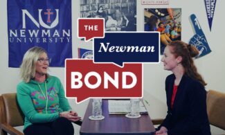 Two alumni sit at a table in front of Newman-themed regalia for an episode of The Newman Bond podcast.