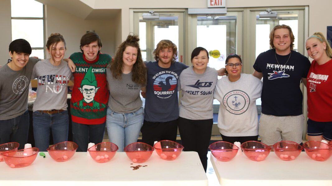 Nine Newman University students stand in line smiling after competing in minute-to-win-it games during Giving Day 2023.