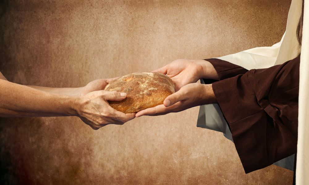 Jesus accepts a loaf of bread from another man's giving hand.