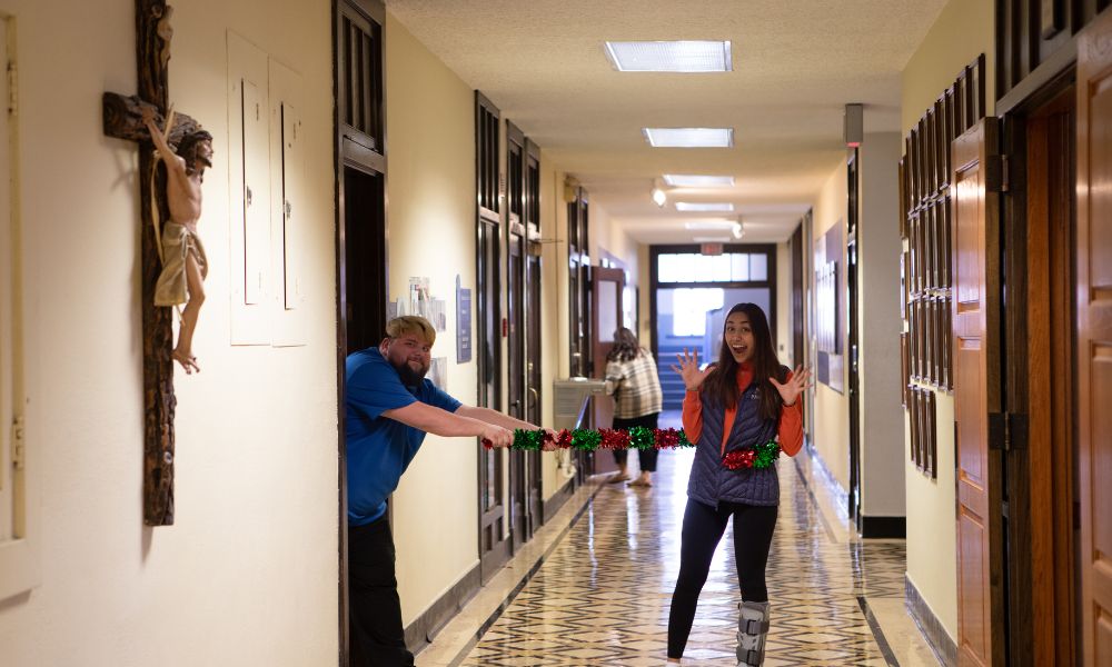 A staff member uses a life-size candy cane to pose with a student in the Sacred Heart Hall main hallway.