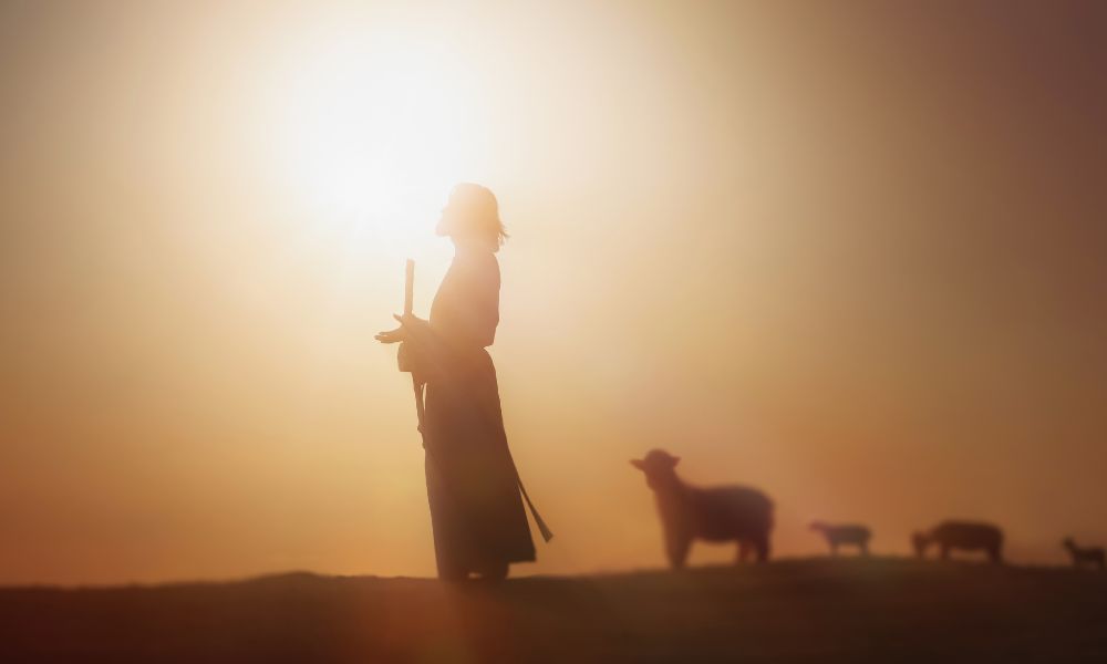 A silhouette of Jesus leading his flock of sheep.