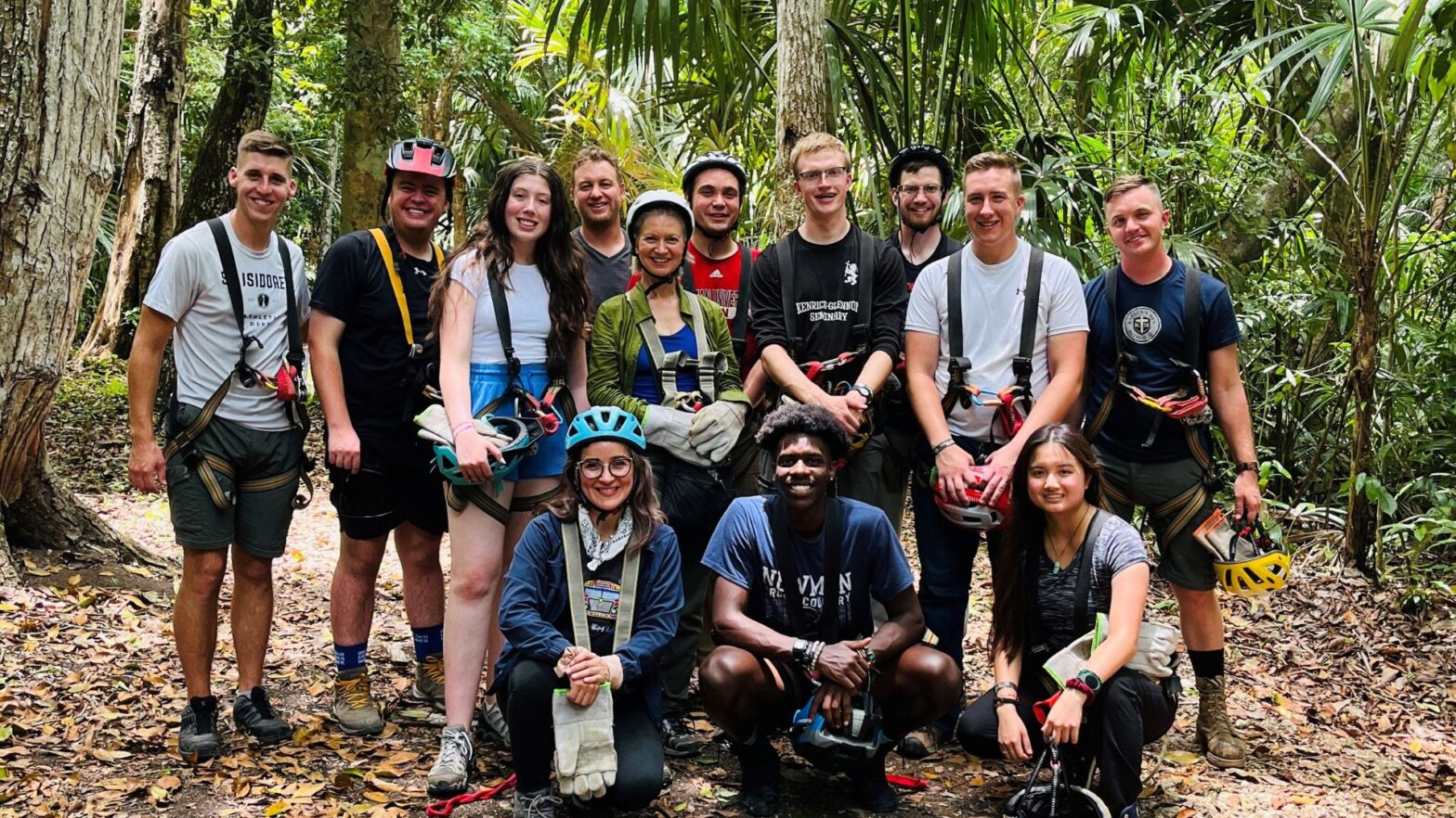 A group photo shows all participants of the 2023 Guatemala Study and Serve program in a jungle. Some are wearing helmets, others are not.