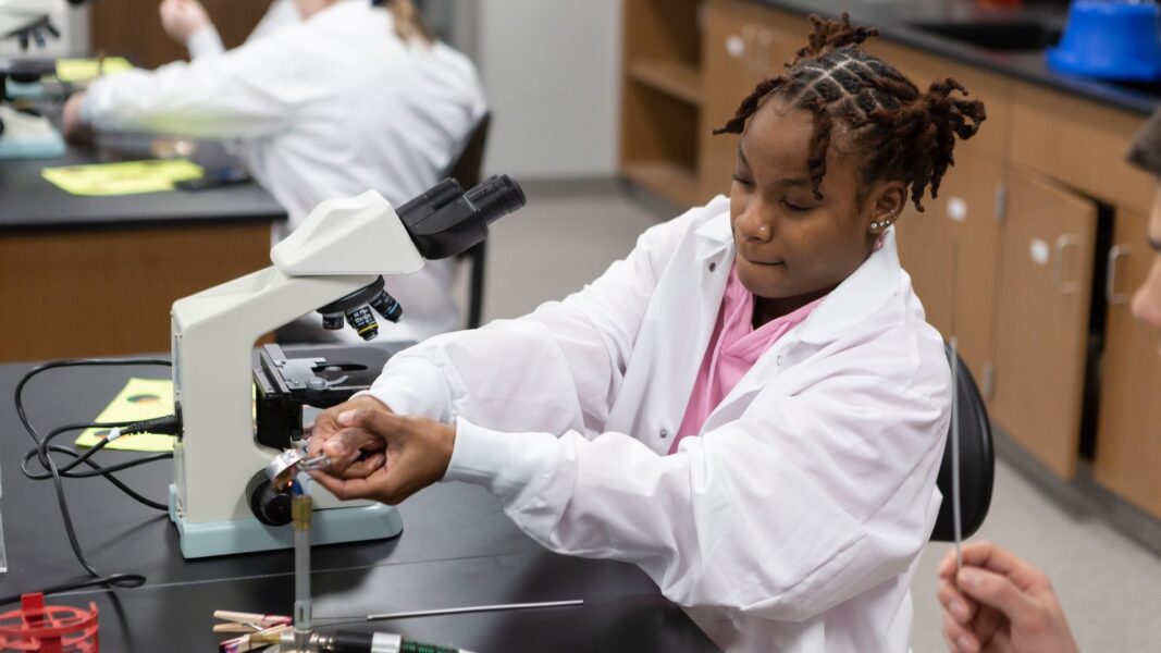 An African American high school student wearing a white lab coat conducts an experiment during NSEP.