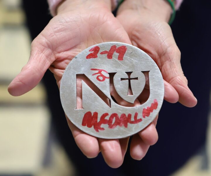 Hands hold up the Newman silver medallion with an "NU" logo carved out.