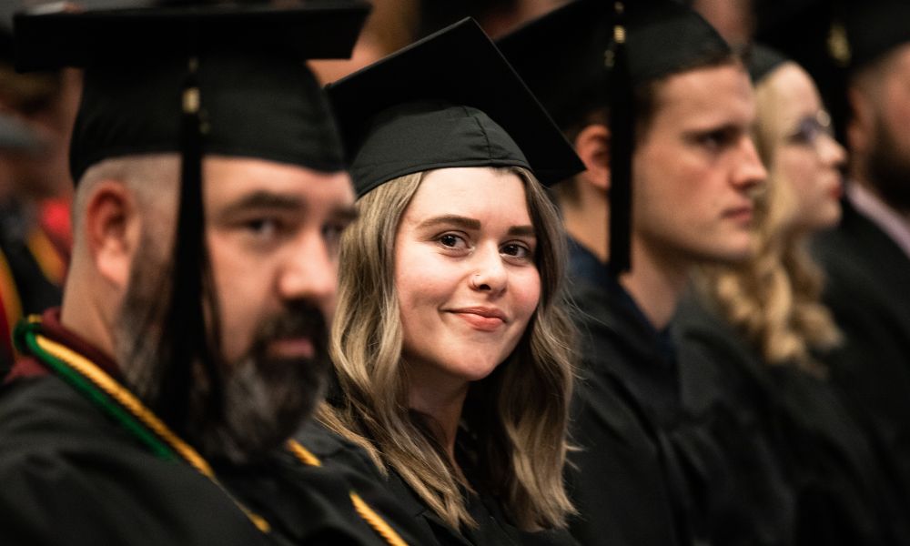 A row of Newman University graduates smile during the 2023 commencement ceremony.