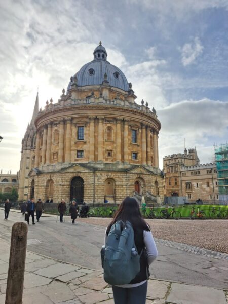 A woman with a backpack stands outside of the Oxford Bodleian Library.