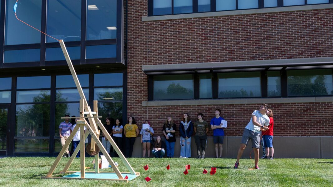 A student launches a trebuchet (catapult) outside the Bishop Gerber Science Center.