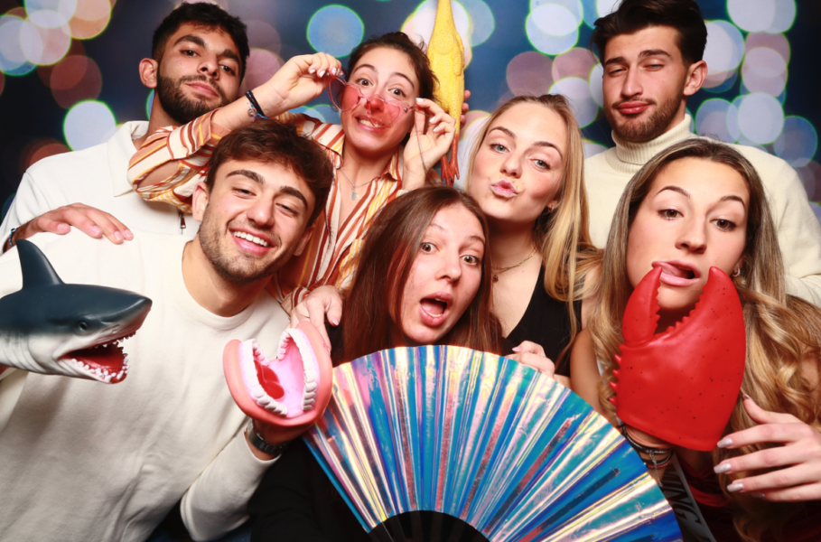 Students use a fan, shark puppet, crab claw, plastic dentures, a rubber chicken and heart-shaped sunglasses as props in the photo booth during the Newman homecoming mixer.