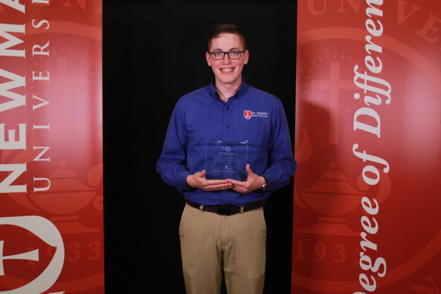 Kuestersteffen holds his award and smiles for a photo on Newman's campus. 