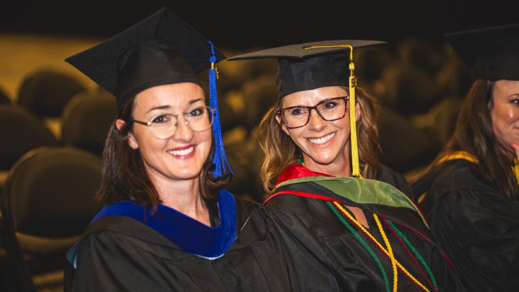 Two Newman graduates smile after moving their tassels from the right to the left, marking the transition from student to graduate.