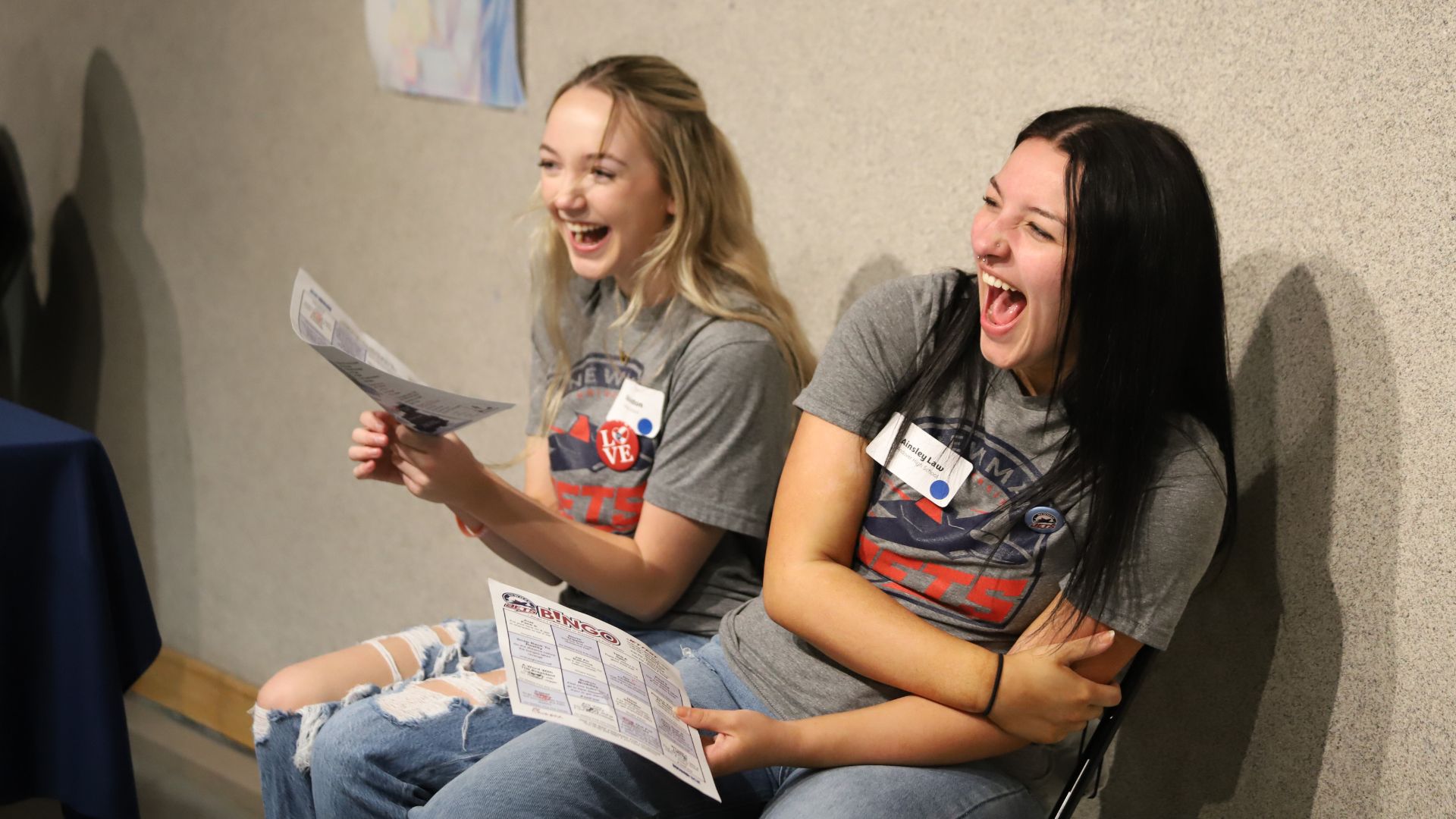 Two female students laugh while holding up caricature artwork from Jet Fest in the spring.