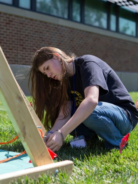 A student prepares a slingshot for a projectile motion activity using a trebuchet.