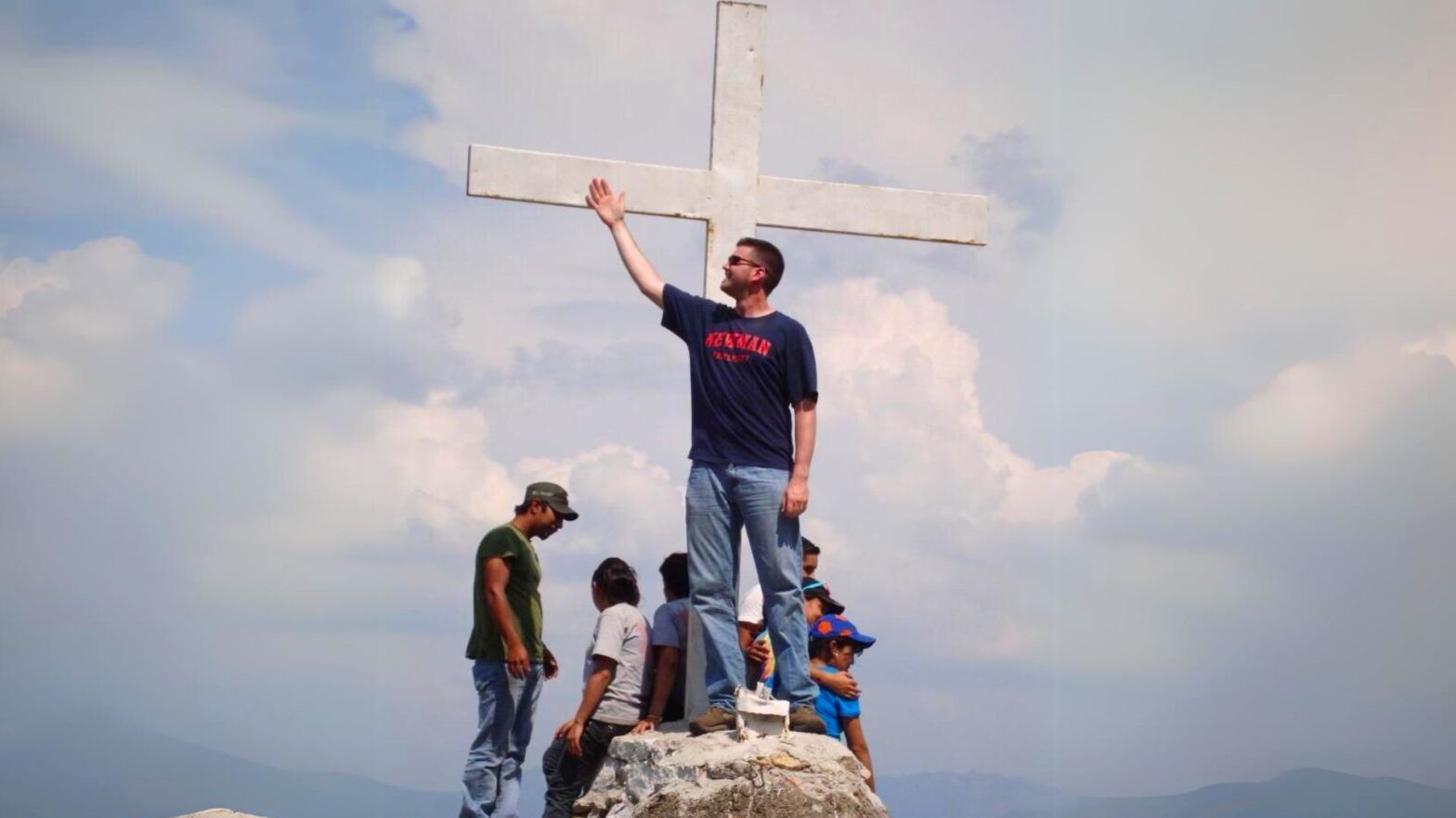 Ralls stands on a rock structure in front of a white cross with fellow participants of the 2012 Guatemala Study and Serve program at Newman University.