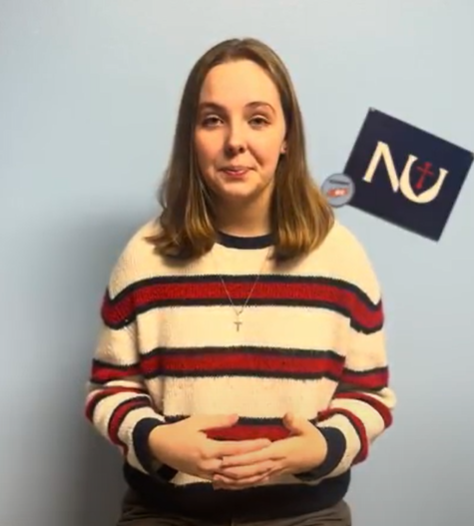 Hertel wears a white and red striped sweater in front of a wall with an "NU" paper cutout behind her.