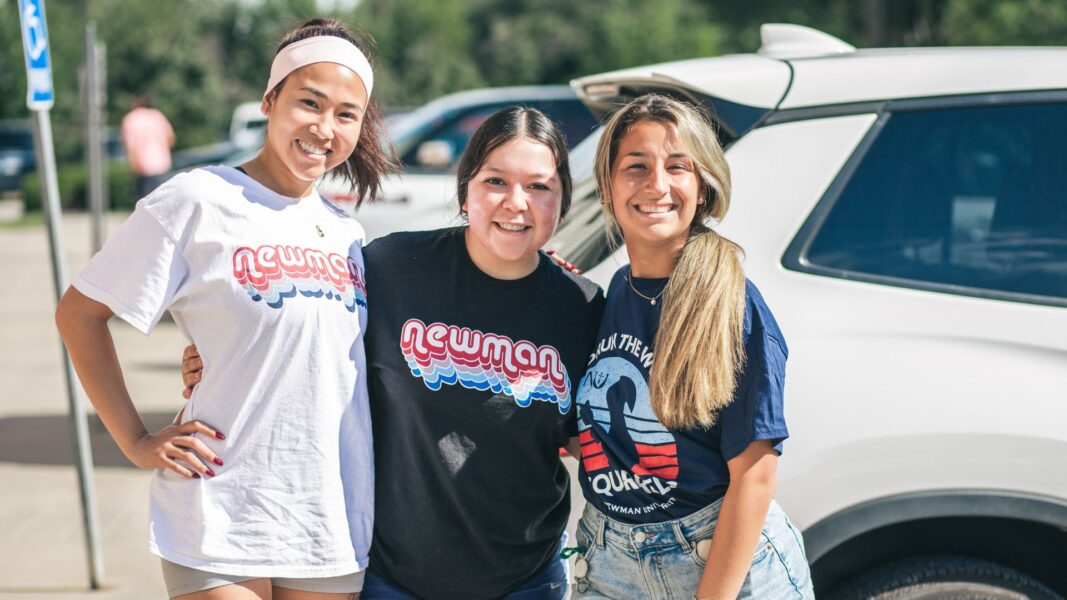 Three female students wear Newman T-shirts on campus at Newman University