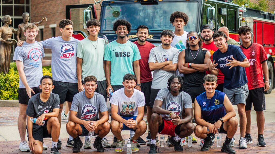 Thomas (back row, white shirt) and members of the men's soccer team stand in front of a firetruck at Founder's Plaza at Newman University.