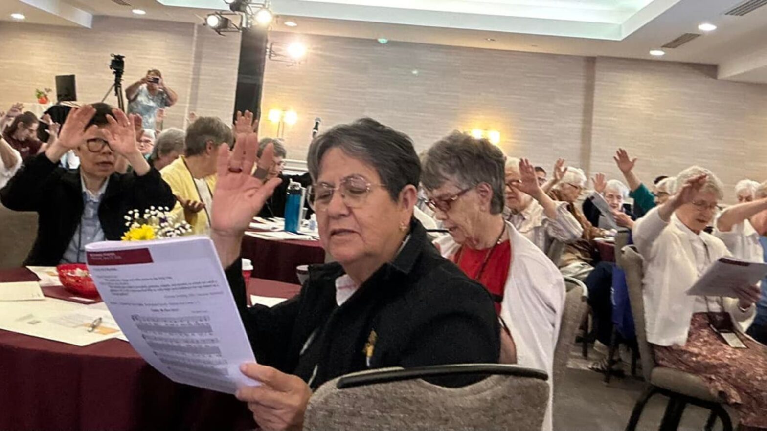 Sisters of the Adorers of the Blood of Christ raise their hands as they read a prayer in unison.