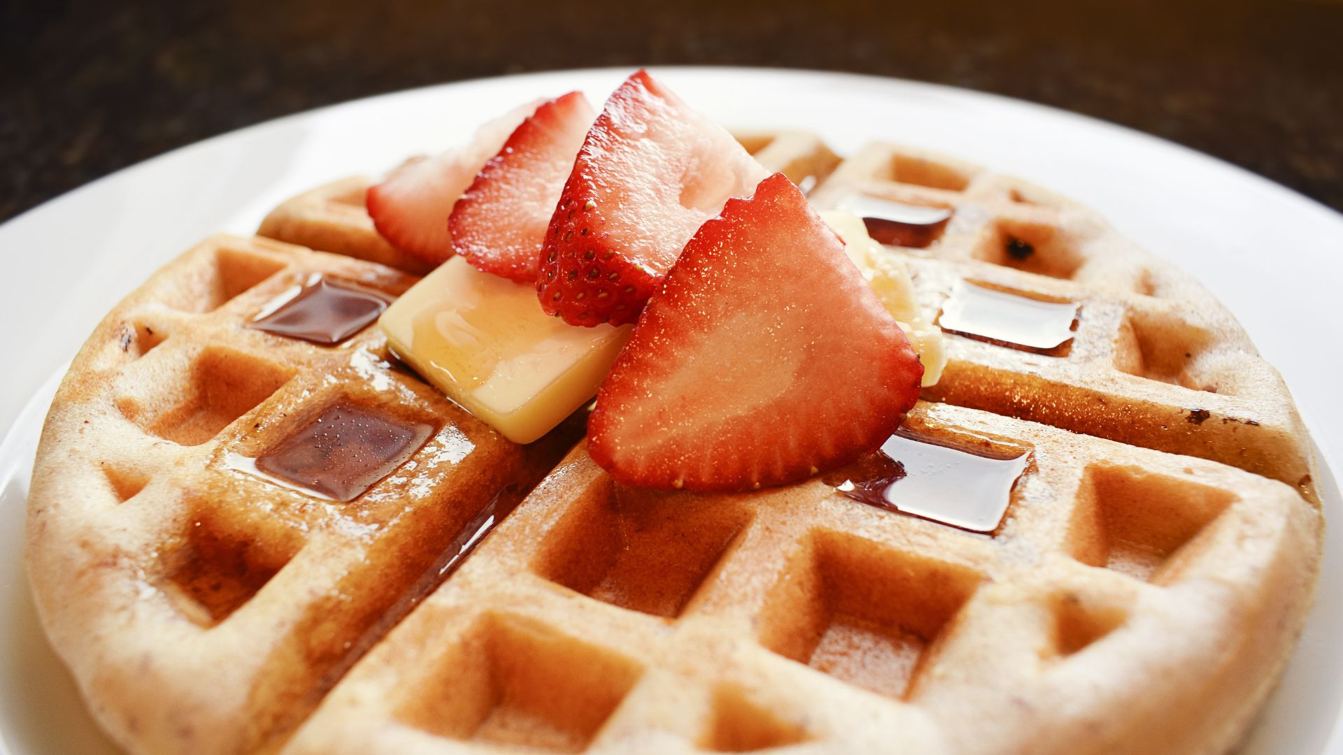 A waffle with strawberries, butter and maple syrup on top.