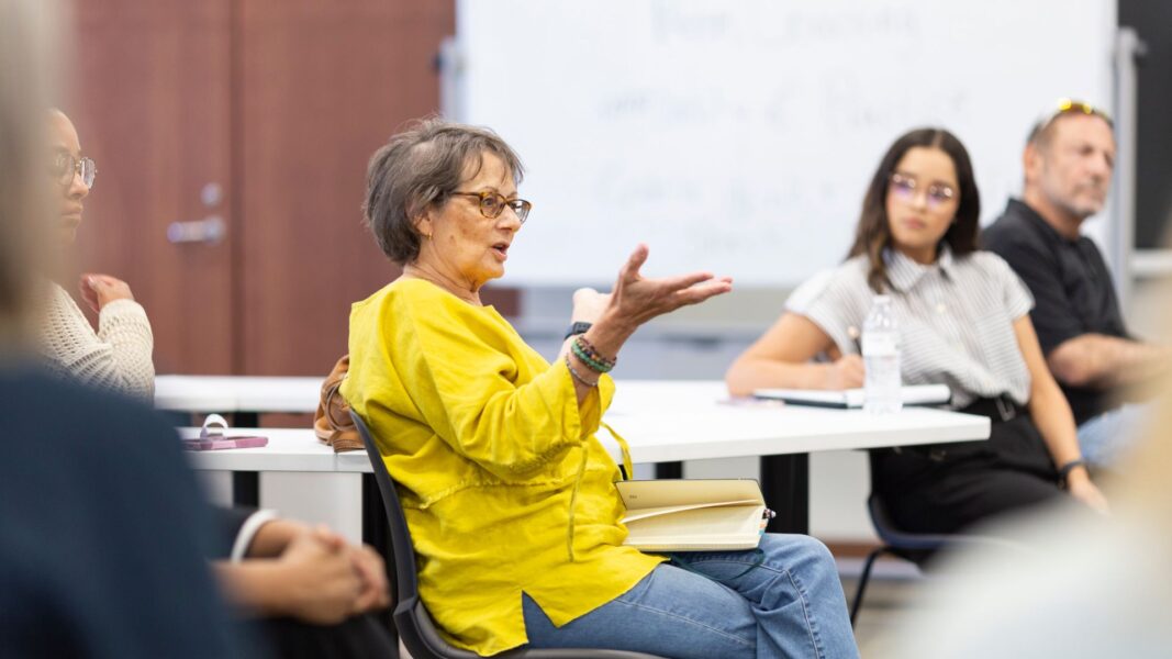 A Newman professor wearing a yellow top speaks to the group of faculty members