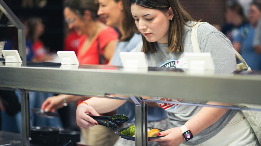 A woman serving herself food through a buffet line