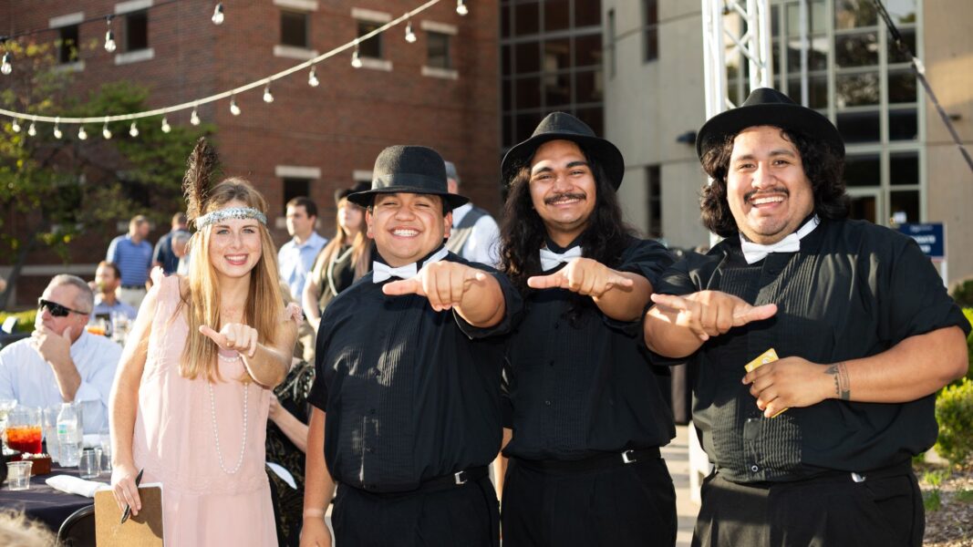 Student performers of the Newman Troubadours hold their hands up in "jet" signs.