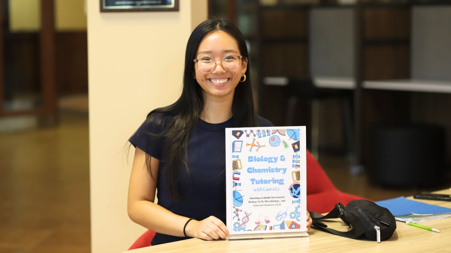 Laura Le shows off her tutor sign at a table in the Student Success Center