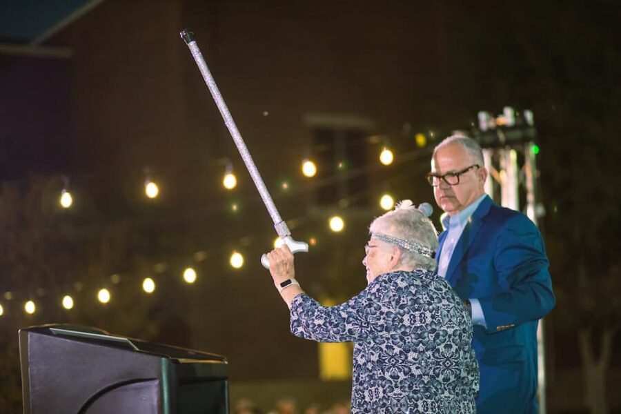 Past Newman president Sister Tarcisia Roths, ASC, hoists her sparkly cane into the air at Party on the Plaza.