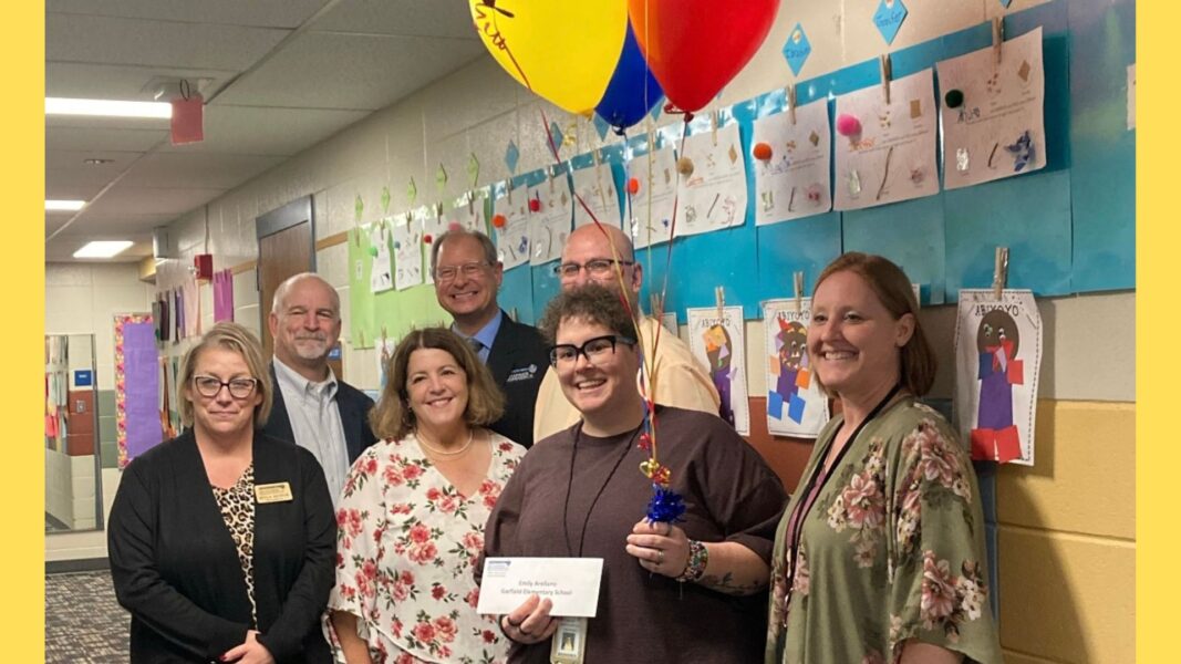 Arellano (center) stands with balloons and an envelope in hand, symbolizing she was selected as a finalist for the Crystal Apple Honor Award.