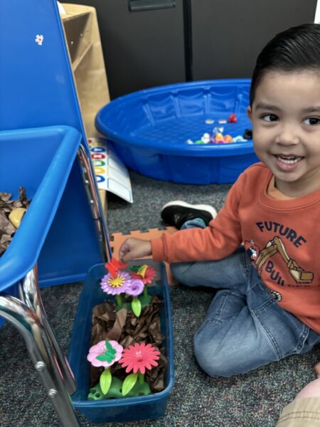 A smiling student tends to a toy flower bed in the classroom.