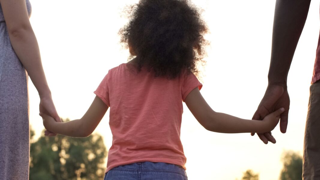 a young girl holds her parents' hands