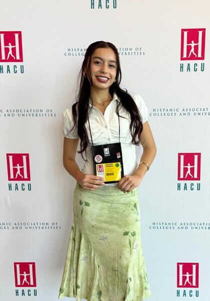 Rosales stands in a white shirt and long green skirt in front of a HACU backdrop at the conference.