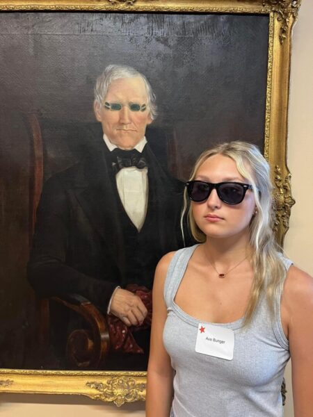 Bunger, in sunglasses, stands next to a painting on the second floor of the Dugan Library.