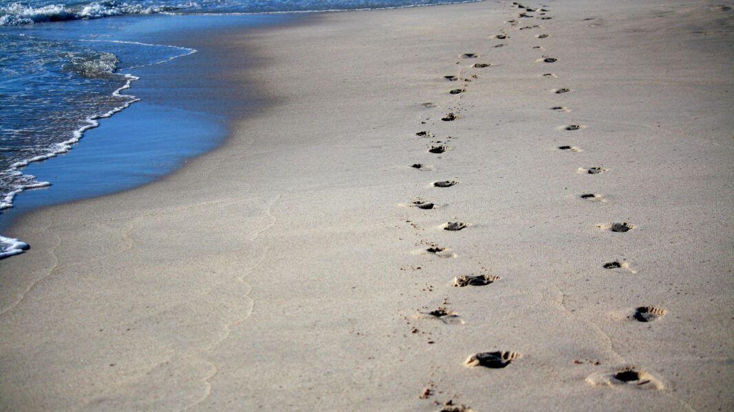 Two sets of footprints line the sand near the ocean