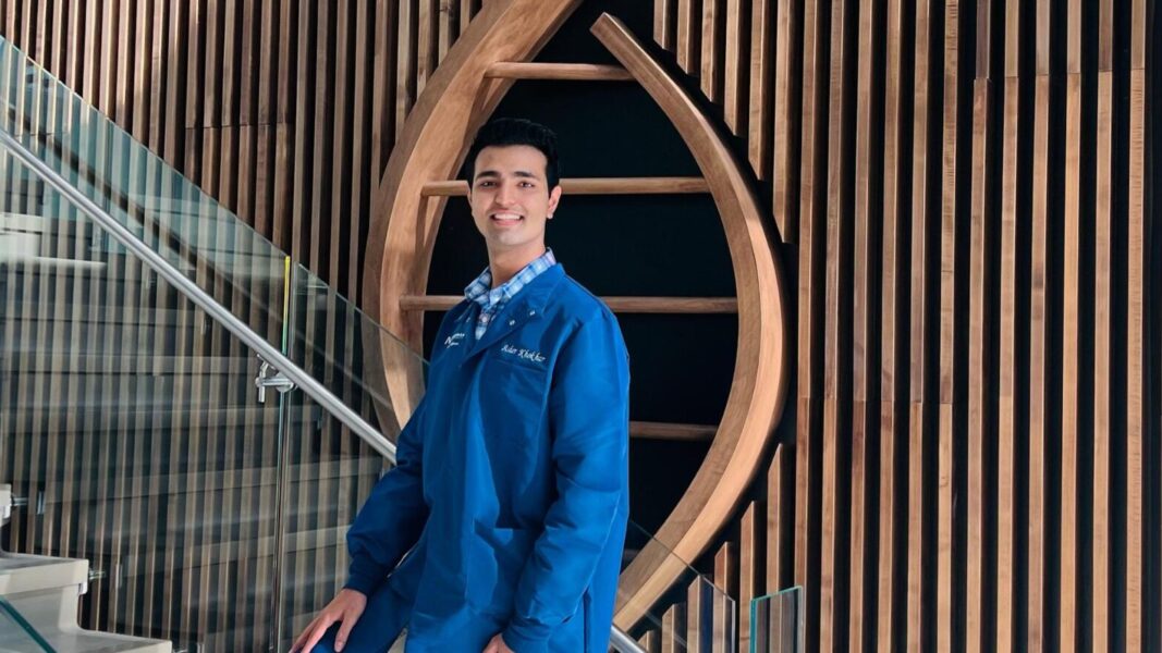 Asher Khokhar stands in front of the wooden DNA strand in the Bishop Gerber Science Center at Newman University.