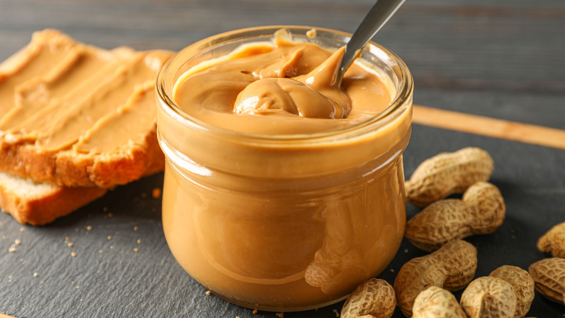 a jar of peanut butter, a peanut butter sandwich, and peanuts