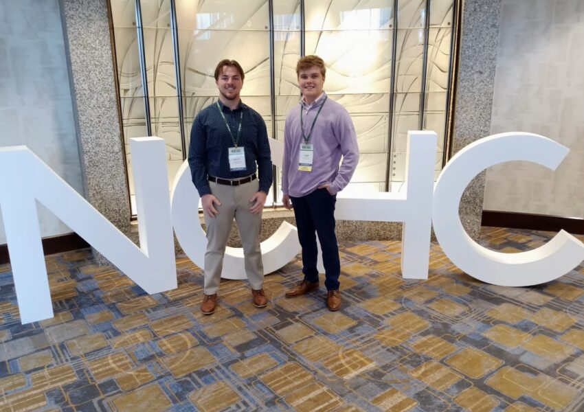 (From left to right) Masem and Davis stand before the "NCHC" letters, short for the National Collegiate Honors Council.