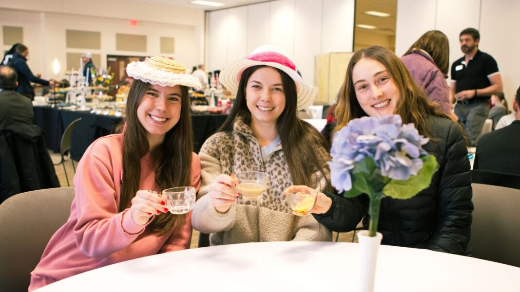 Three Newman students hold up their tea in "cheers" during High Tea.