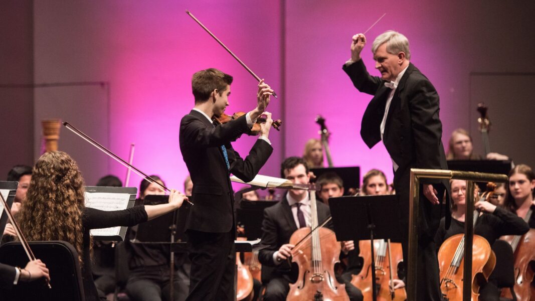 Roy stands before the director during a performance